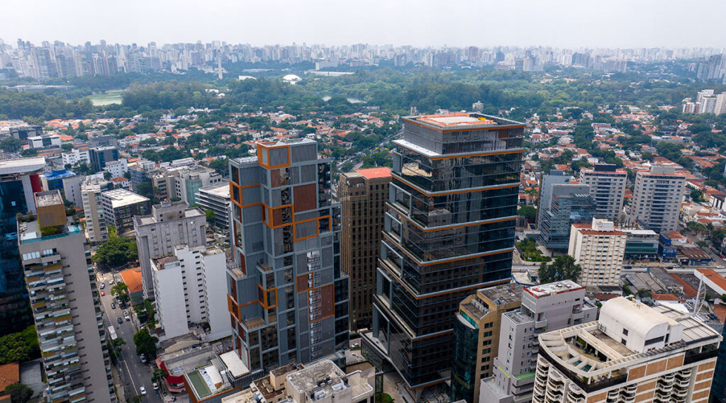 Vista aérea do JK Square Corporate em São Paulo, destacando a torre corporativa envidraçada com linhas horizontais e volumetria escalonada, em meio ao eixo urbano e arborizado da cidade.